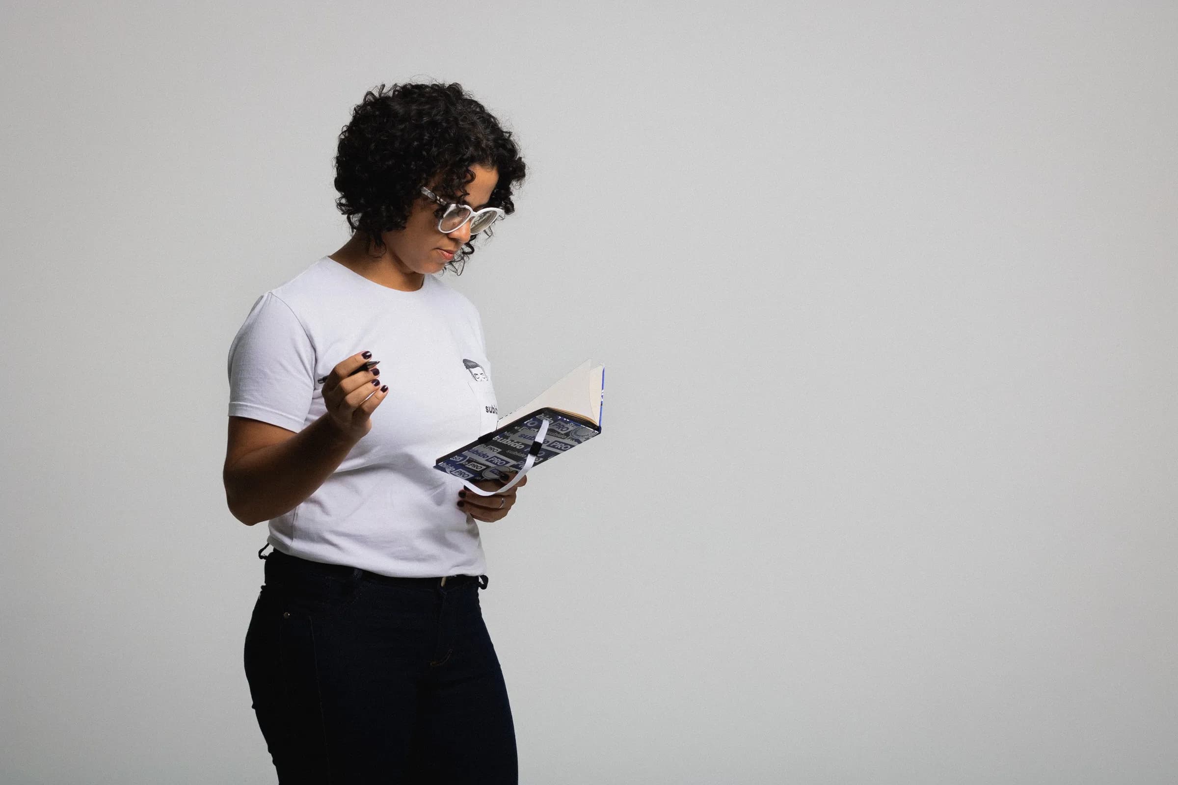 Fernanda Lira lendo um caderno de anotações, em estúdio de fundo claro